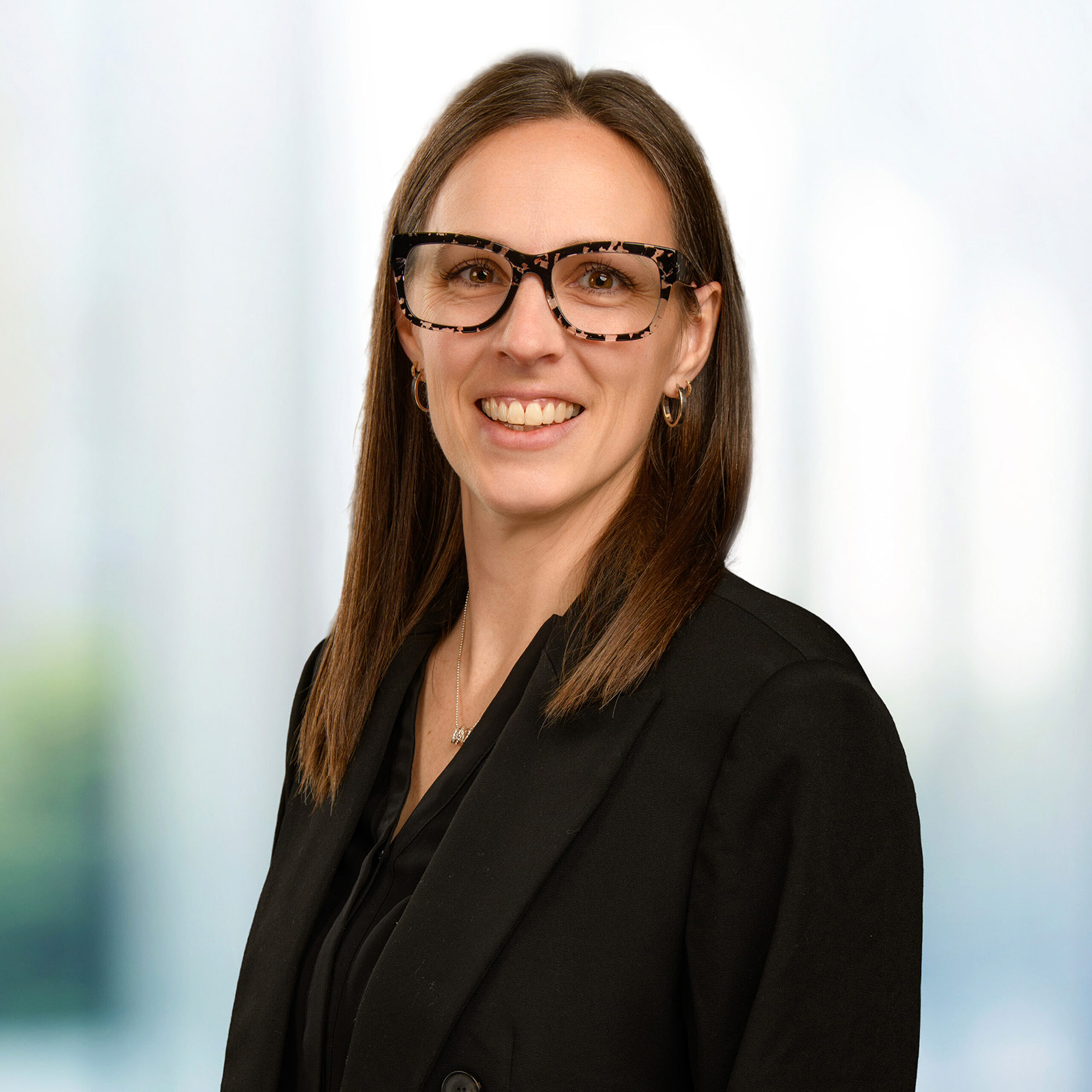 Smiling woman wearing tortoiseshell glasses and a black blazer with shoulder-length brown hair.