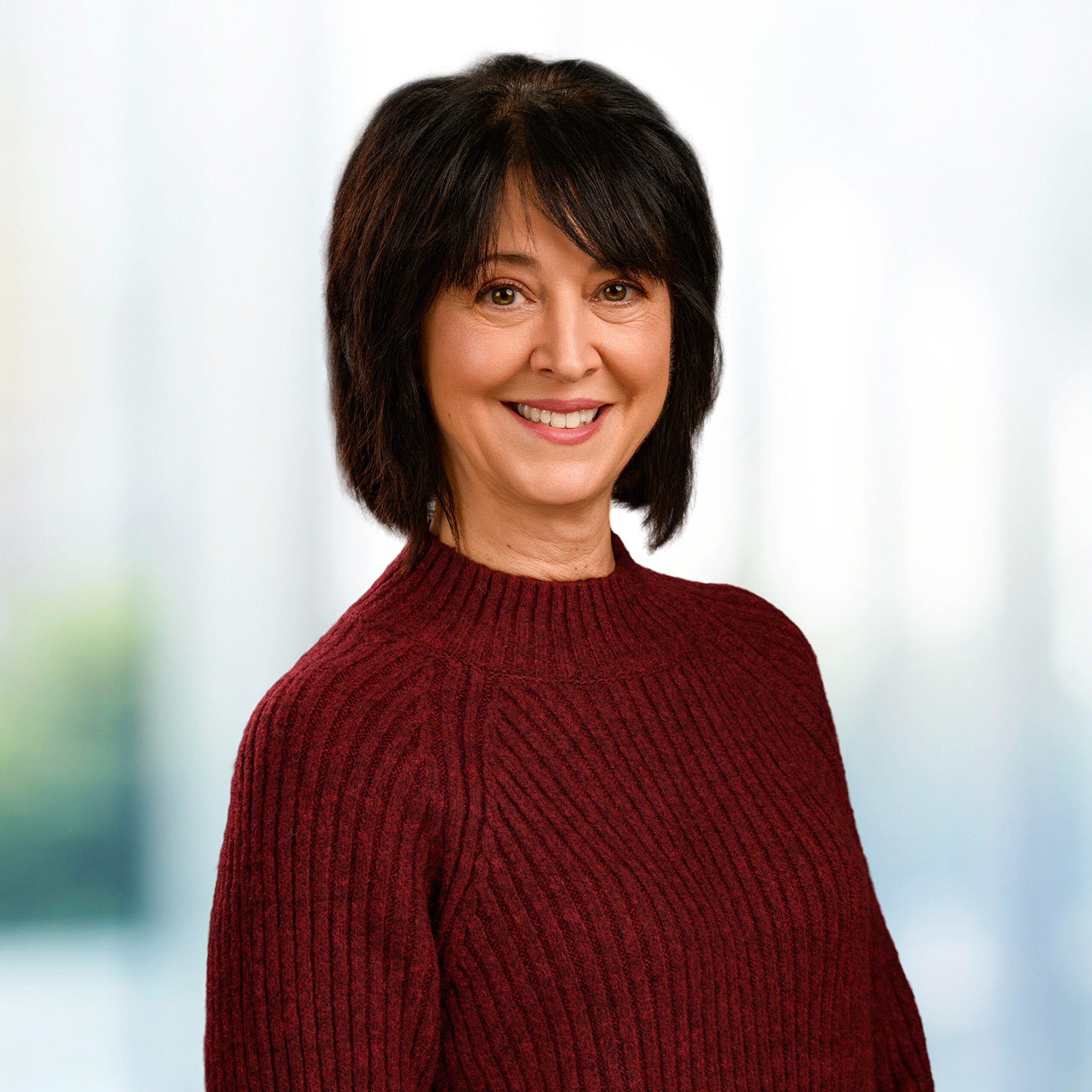 Woman with dark shoulder-length hair smiling, wearing a maroon ribbed sweater against a soft blurred background.