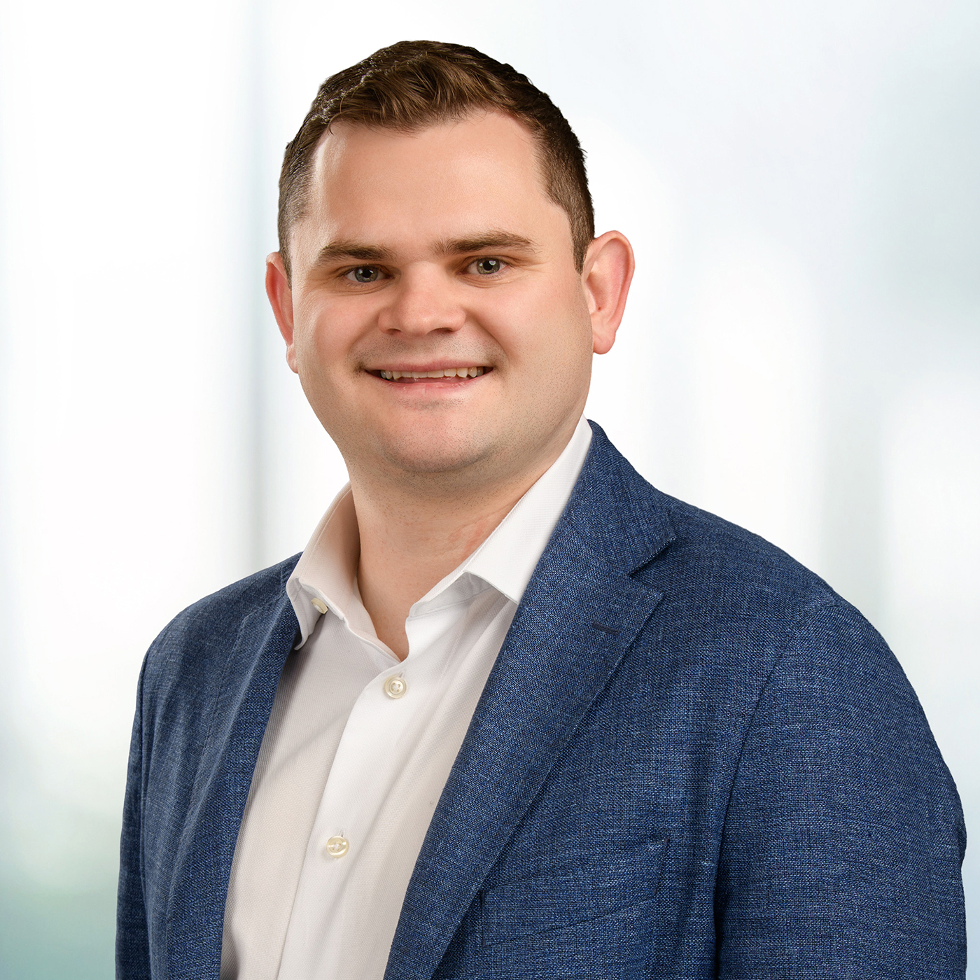 Smiling man in a blue blazer and white shirt with short dark hair, posed against a soft light background.