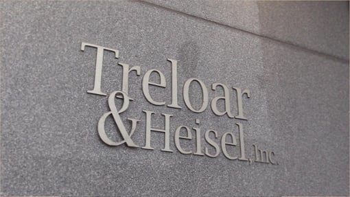 Raised metal company sign reading Treloar & Heisel, Inc. mounted on a textured gray stone wall.